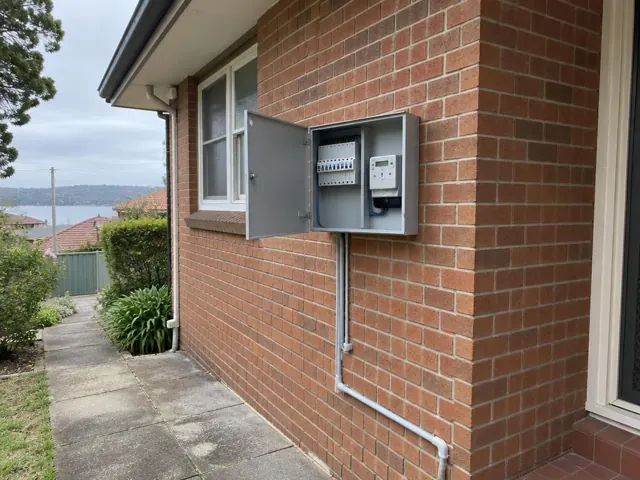 Open exterior switchboard on a brick house wall beside a window and pathway in Gosford